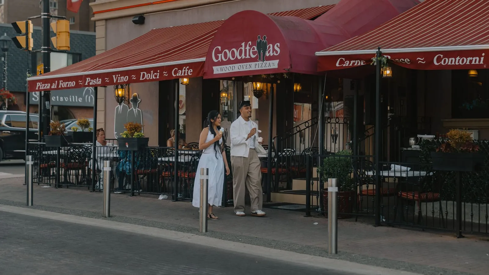 Dev and his sister walking past the Goodfellas Wood Oven Pizza patio with ice cream