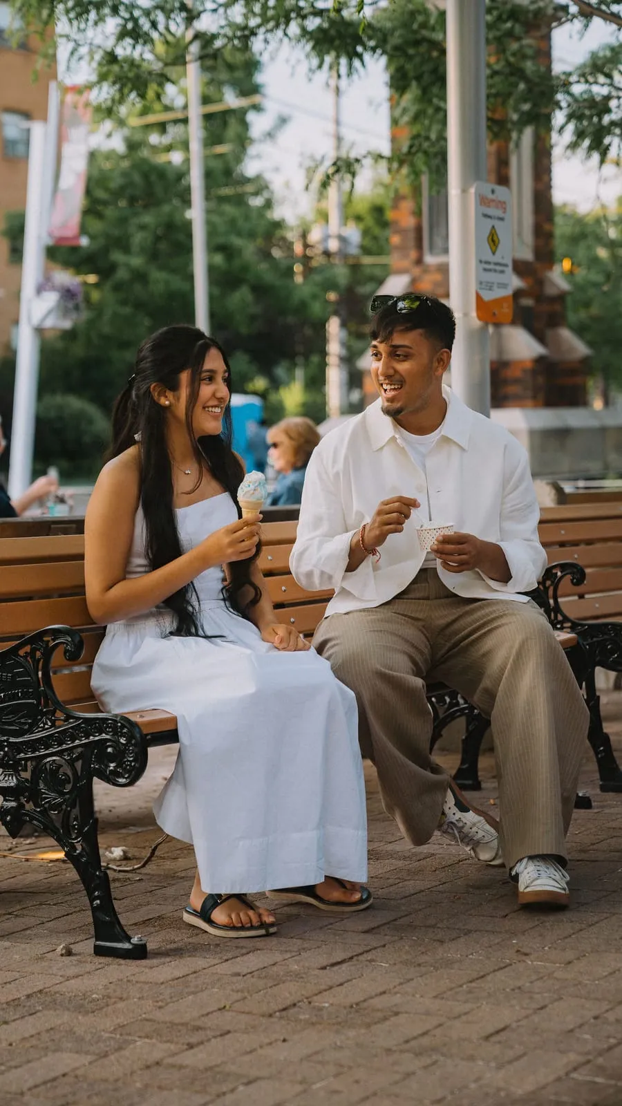 Dev and his sister laughing over ice cream on a bench in the Streetsville core